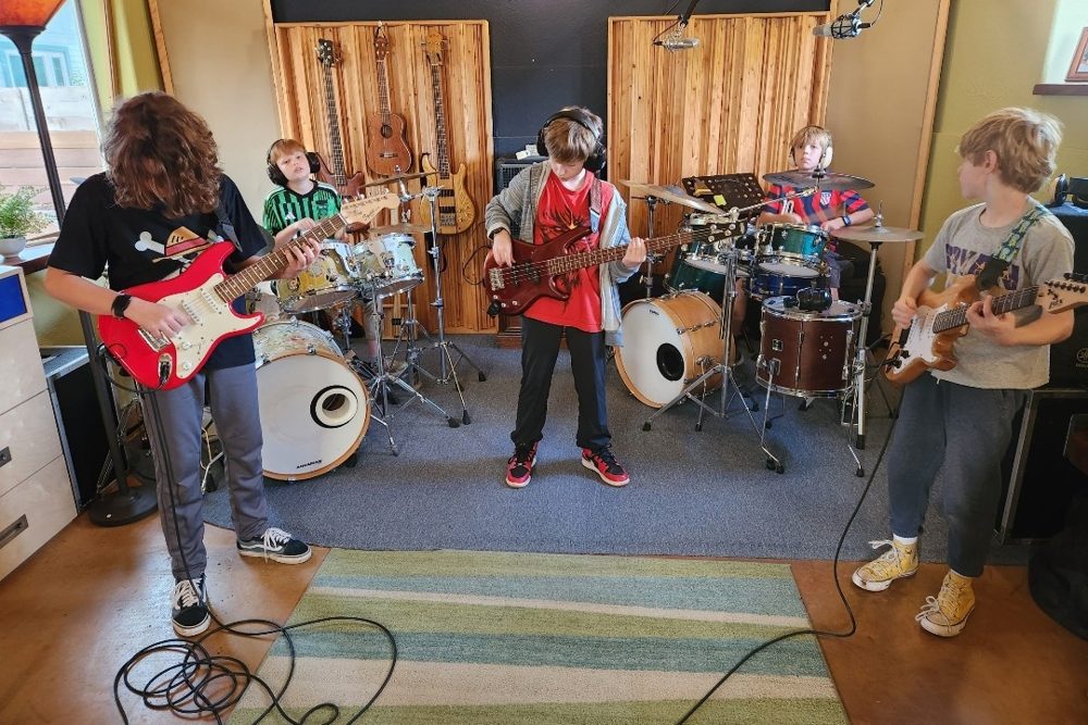 Students playing guitar, bass and drums together in a band during a lesson