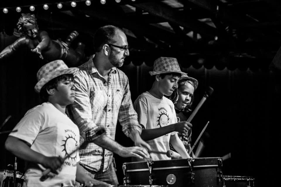 A drum teacher and students playing drums together on stage