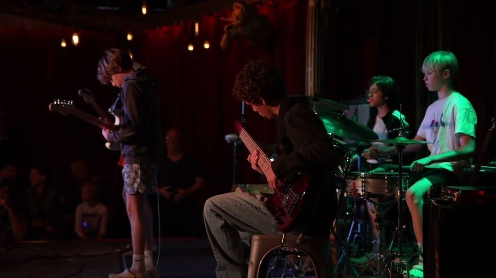 A student drummer playing in a band on stage at a student show