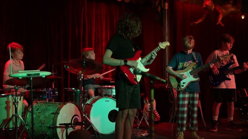Two students on drum kits playing in a band on stage at a student show